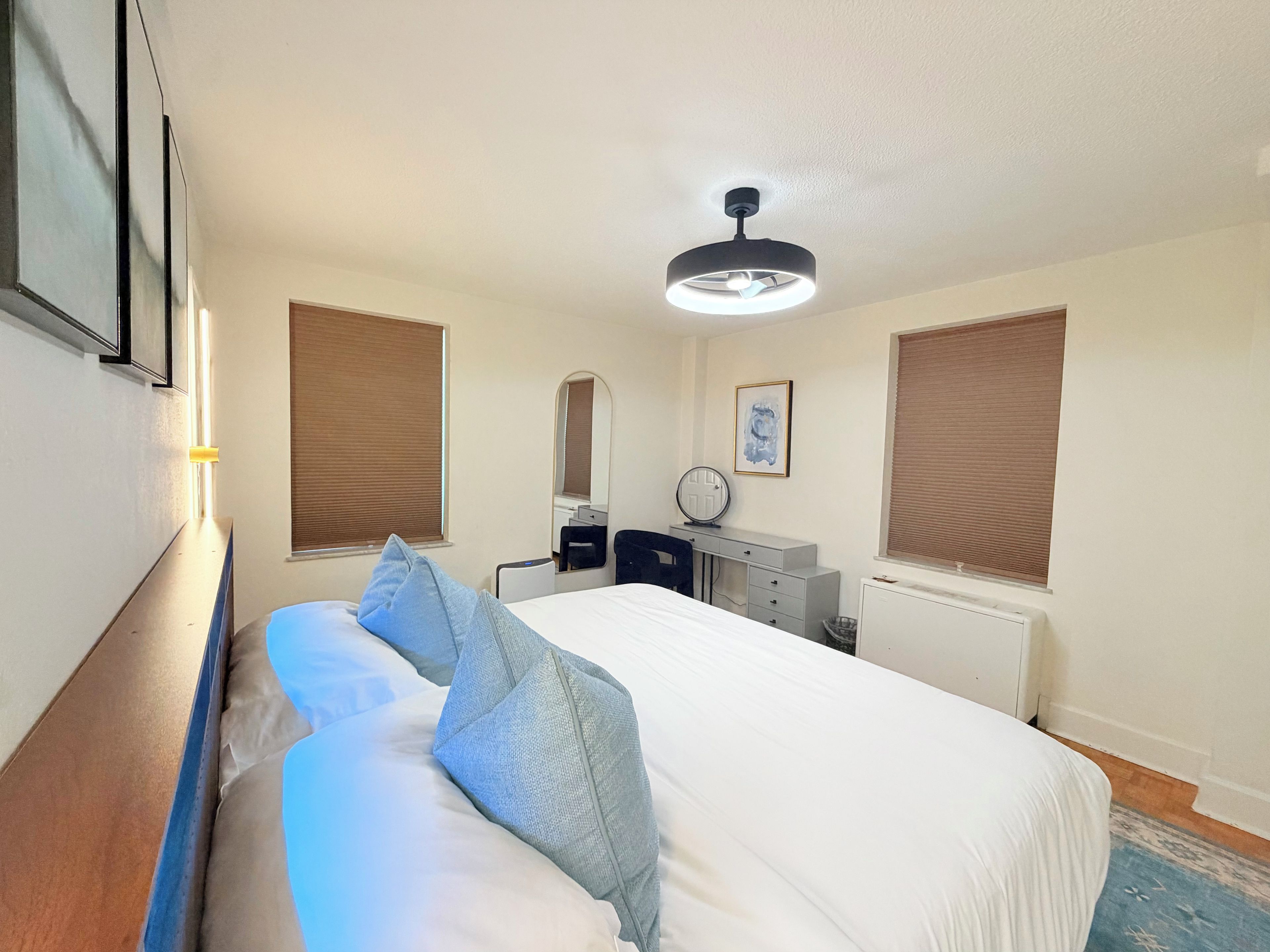 A hotel room with a bed, bedside table, mirror, dresser, and a ceiling fan.
