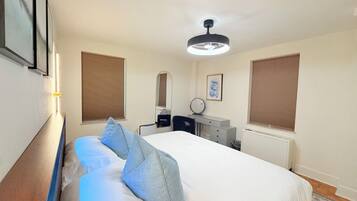 A hotel room with a bed, bedside table, mirror, dresser, and a ceiling fan.