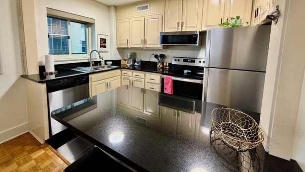 A modern kitchen with a central island, stainless steel appliances, and light-colored cabinetry. - Come enjoy a cozy, spacious high-rise condo with breathtaking sunset views. (Atlanta)