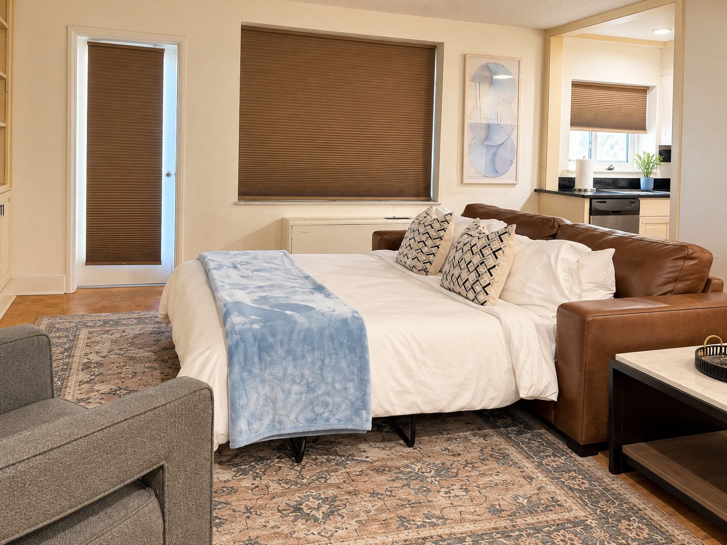 A bedroom with a bed, a sofa, a coffee table, a rug, and a kitchen area in the background.