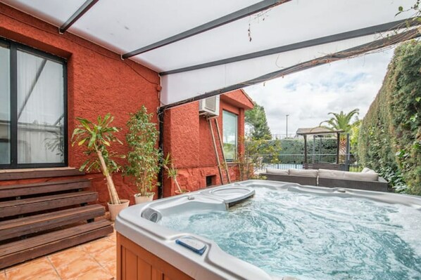 An outdoor hot tub area with a wooden bench and potted plants.