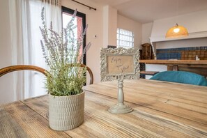 A wooden dining table with a textured vase of green plants, a decorative sign, and a blue chair.