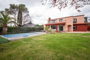 A modern two-story house with a swimming pool, surrounded by a well-maintained lawn and a metal fence.