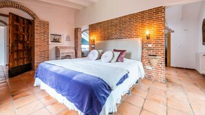 A bedroom with a brick wall, a bed with a white headboard, and a white bench.