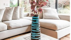 A living room with a beige sofa, a patterned coffee table, and a vase with red foliage.