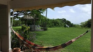 A hammock on a balcony overlooking a grassy area with a thatched-roof structure in the background. - Villa Lagoon Accès Direct à la mer (Le Vauclin)