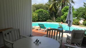 A patio with a round table and white chairs, overlooking a swimming pool and lush greenery. - Villa Lagoon Accès Direct à la mer (Le Vauclin)