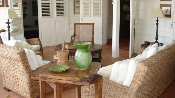 A cozy room with wicker furniture, a wooden table, and a green vase. - Villa Lagoon Accès Direct à la mer (Le Vauclin)