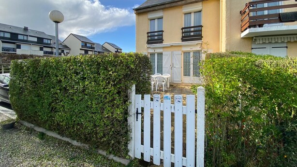 A residential building with a white picket fence, a balcony, and a small patio area with outdoor furniture.