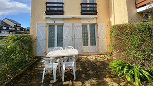 A two-story building with a patio area featuring a table and chairs, a covered outdoor seating area, and a small garden.