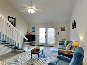 Ein Wohnzimmer mit Treppe, Fernseher, Sofa, Couchtisch und Deckenventilator.