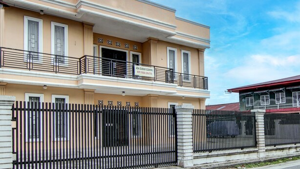 A two-story building with a balcony, a gated entrance, and a sign indicating it is a free guest house.