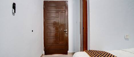 Quarto de hotel com porta de madeira, cama com colcha estampada e parede branca com tomada.