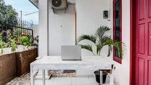A small outdoor area with a white table, a laptop, and a red door.