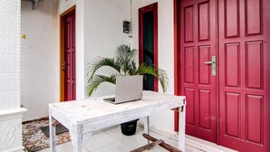 A white table with a laptop, a red door, and a potted plant in a narrow outdoor space.