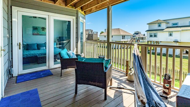 A wooden deck with a sliding glass door leading to a bedroom, a wicker chair, and a hammock.