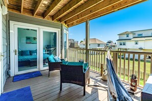 A wooden deck with a sliding glass door leading to a bedroom, a wicker chair, and a hammock.