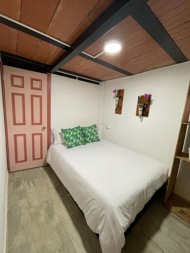 A single-bed room with a wooden ceiling, a white bedspread, and a pink door.