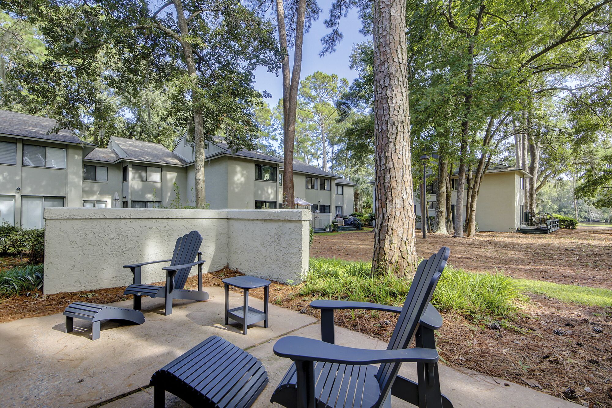 A courtyard with outdoor seating, including chairs and a table, surrounded by trees and a building with multiple windows.