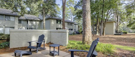 A courtyard with outdoor seating, including chairs and a table, surrounded by trees and a building with multiple windows.