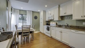 Une cuisine moderne avec des meubles blancs, un plan de travail en granit et un coin repas comprenant une table et des chaises.