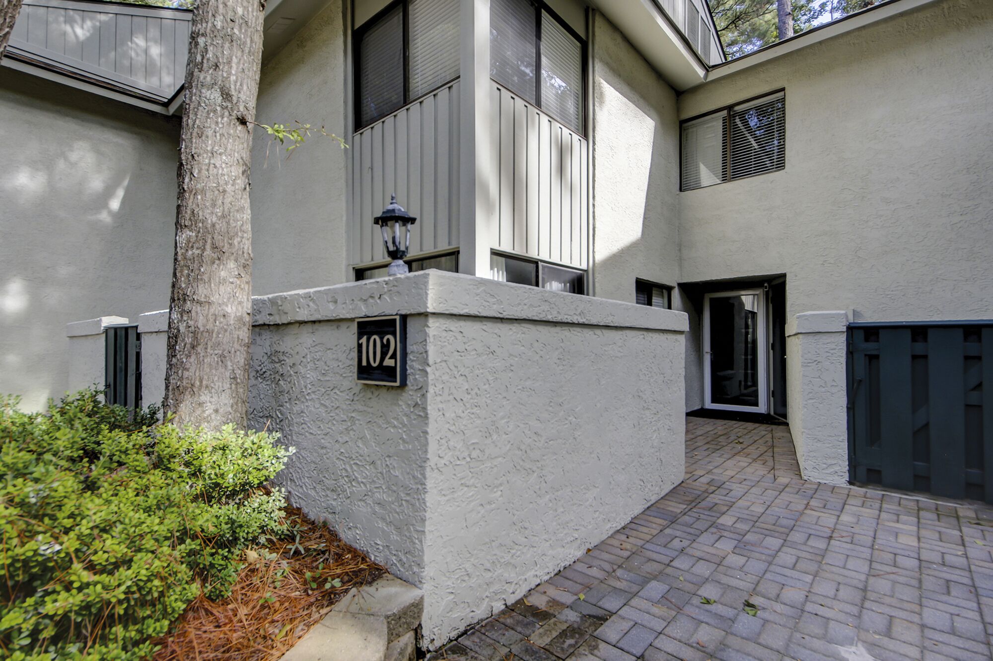A modern building with a white exterior, a number '102' sign, and a paved entrance area.