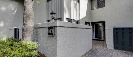 A modern building with a white exterior, a number '102' sign, and a paved entrance area.
