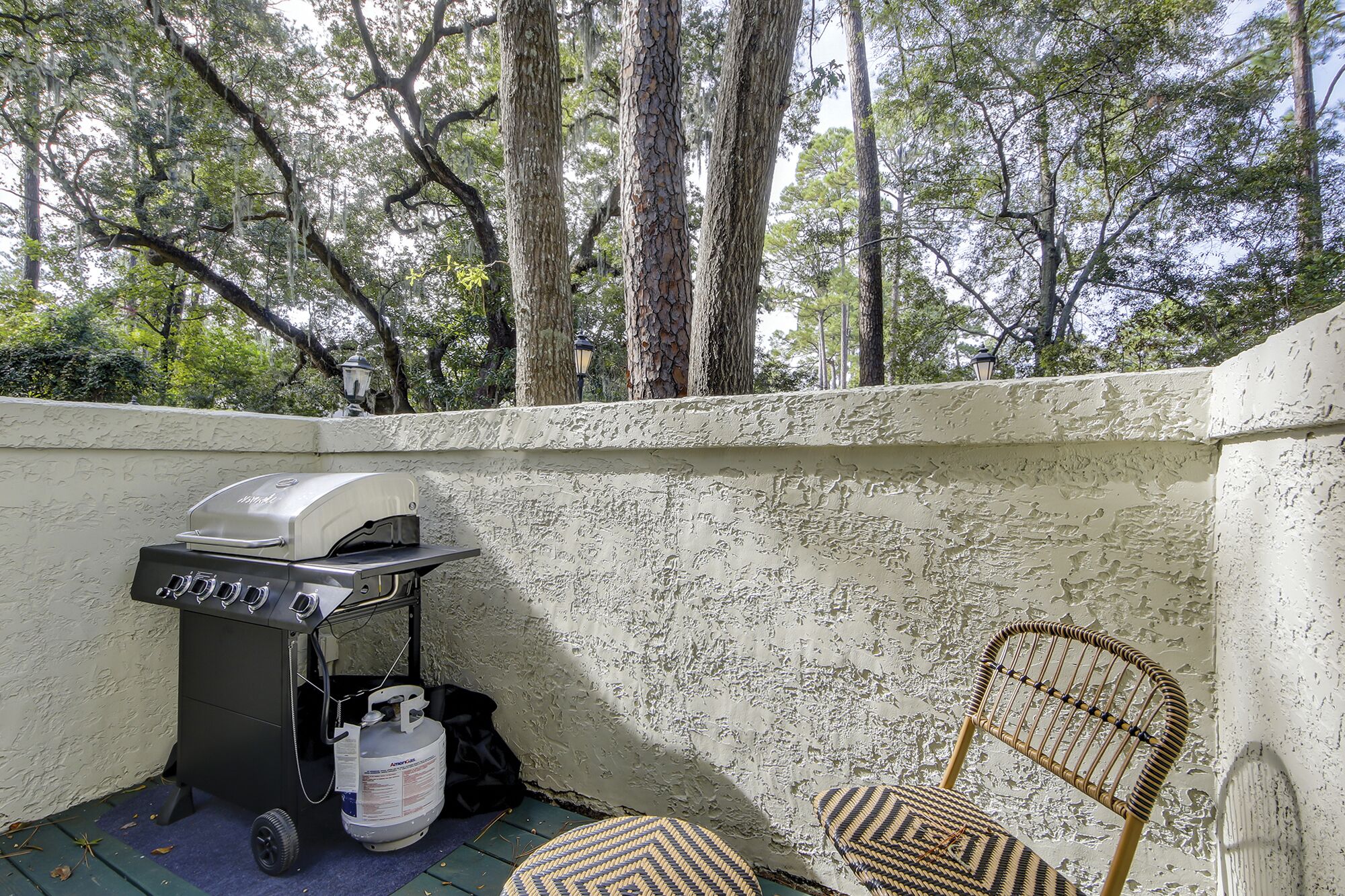 A patio with a grill, a gas tank, and a wicker chair.