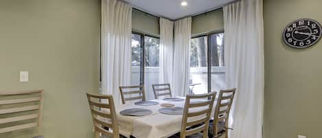 A dining area with a round table, six chairs, and a clock on the wall.