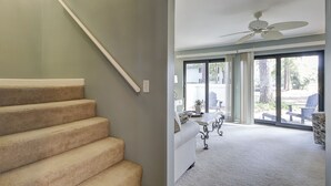 Un escalier menant à une pièce dotée d’un ventilateur de plafond, un coin repas avec des sièges en plein air et une vue sur l’extérieur.