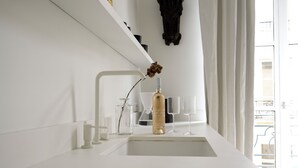 Una cocina moderna con encimera blanca, grifo dorado y un florero con flores secas.