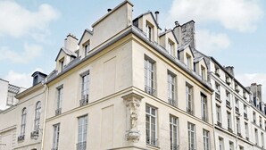 Un edificio de varios pisos con un estilo arquitectónico clásico, que presenta ventanas simétricas y detalles decorativos en la fachada.