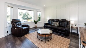 Una sala de estar con piso de madera oscura, un sofá de cuero, un sillón reclinable de cuero y una mesa de centro redonda.