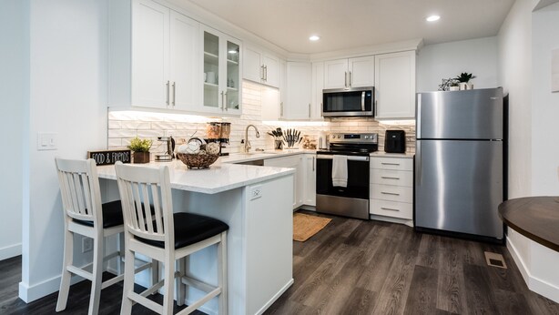 Una cocina moderna con armarios blancos, un refrigerador de acero inoxidable y una isla central con taburetes de bar.