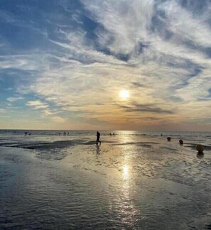 Een strand met mensen die wandelen, de zon die ondergaat en een rustige zee.