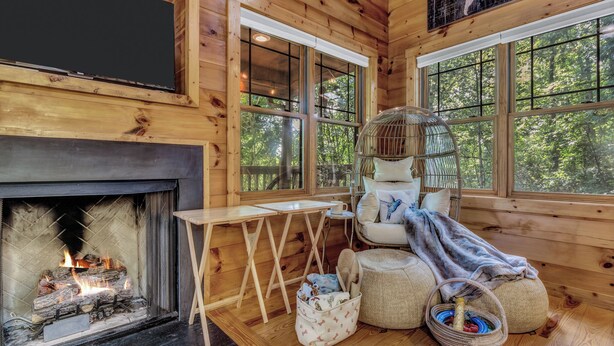 L’intérieur d’un chalet accueillant, avec une cheminée, des murs en bois, de grandes fenêtres, une petite table et des sièges confortables.