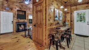 Un intérieur en bois avec une cheminée, un coin repas et un téléviseur fixé au mur.