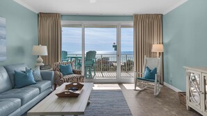 A living room with a sofa, chairs, a coffee table, and a view of the ocean through large sliding doors.