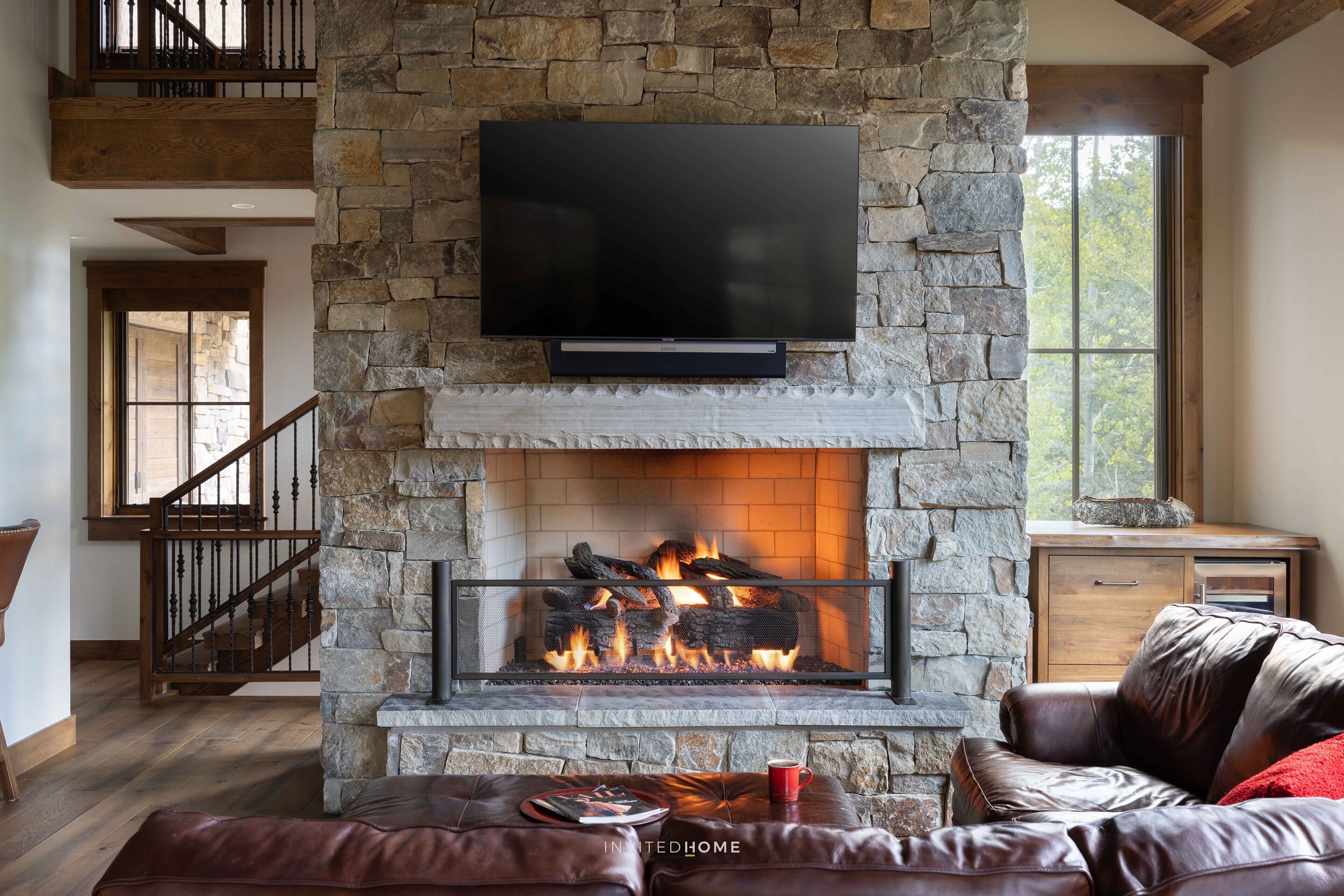 A stone fireplace with a TV mounted above it, a leather sofa, and a staircase with wooden railings.