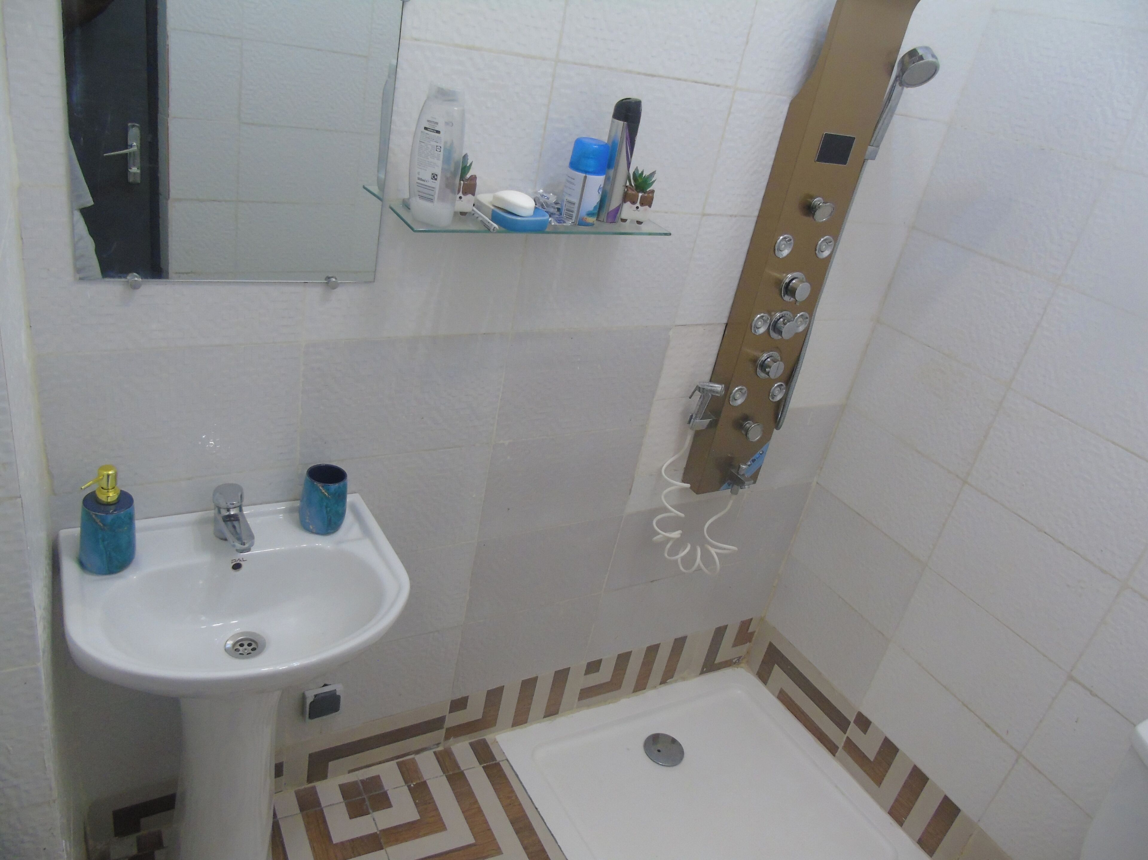 Ein Badezimmer mit einem weißen Waschbecken, einer Dusche mit mehreren Armaturen und einem Spiegel über dem Waschbecken.
