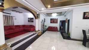 Un amplio salón con sofás rojos, un pilar decorativo y suelo de baldosas.