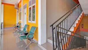 Un couloir avec un escalier, des chaises et un extincteur.