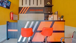 Un espace d’accueil au design moderne, comprenant un comptoir de réception, deux tabourets de bar orange et un extincteur fixé au mur.