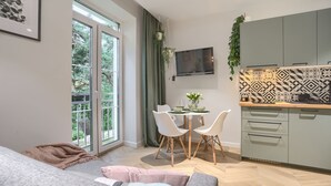 A modern kitchen with a dining area, a flat-screen TV, and a view of greenery outside. - Apartamenty Sun & Snow Las i Morze (Trzebiatow)