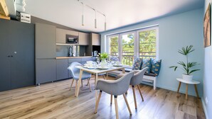 A modern kitchen with grey cabinets, a dining table set with chairs, and a window with a view of trees. - Apartamenty Sun & Snow Las i Morze (Trzebiatow)