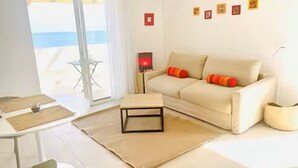 Un salon moderne avec un canapé, une petite table, une lampe et une vue sur la mer, visible à travers une porte vitrée.