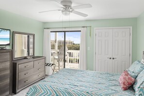 Enjoy a room with a balcony offering views of the surrounding area, a bed, dresser, and ceiling fan.