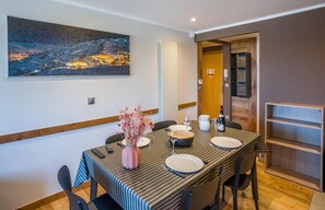 A dining area with a long table, chairs, a vase with flowers, and a painting on the wall.