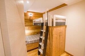 A bunk bed with a wooden wardrobe and a small bench.