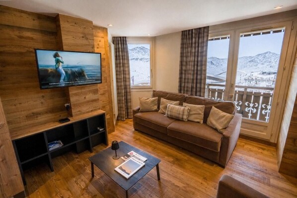 A living room with a wooden wall, a brown sofa, a coffee table, and a TV mounted on the wall.